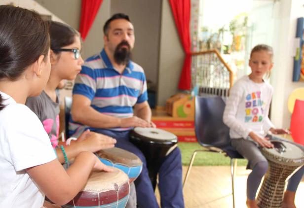 Eine Gruppe von Kindern und ein Mann spielen auf Trommeln in einem Raum.