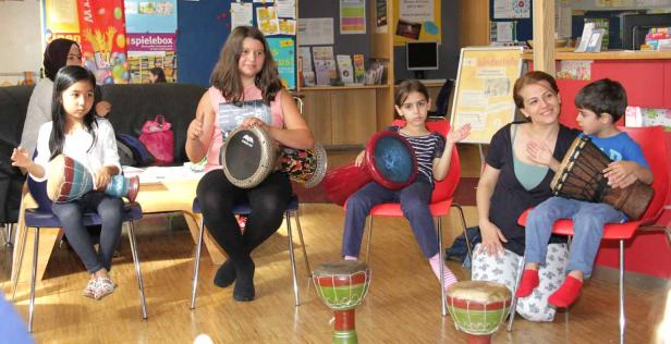 Eine Gruppe von Kindern und Erwachsenen sitzt mit Trommeln in einem Raum.
