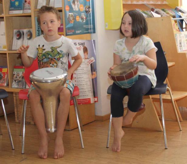 Ein Junge und ein Mädchen sitzen auf Stühlen und spielen Trommeln.