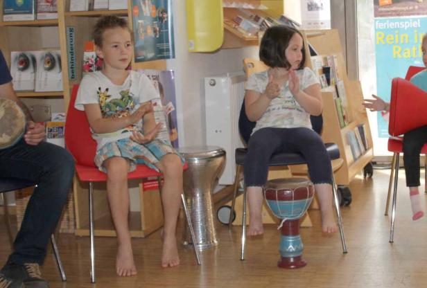 Zwei Kinder sitzen auf Stühlen und spielen auf Trommeln.