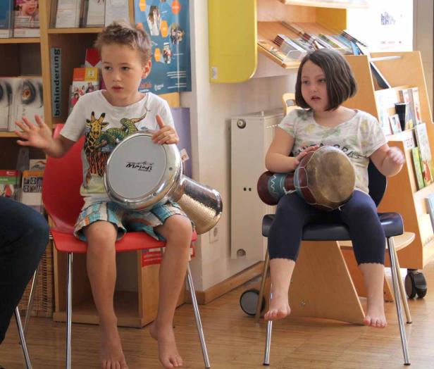 Zwei Kinder sitzen auf Stühlen und spielen auf ihren Trommeln.