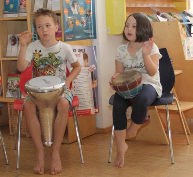 Ein Junge und ein Mädchen sitzen auf Stühlen und spielen auf Trommeln.