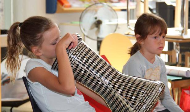 Ein Mädchen spielt auf einer verzierten Trommel, während ein anderes Mädchen zusieht.