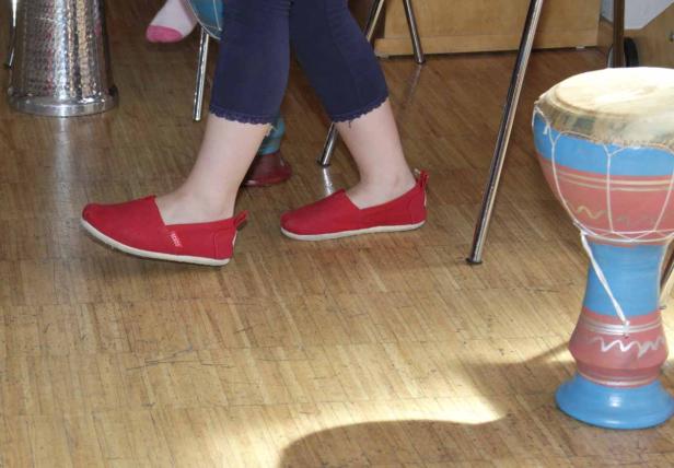 Eine Person mit roten Schuhen steht neben einer Trommel auf einem Holzboden.