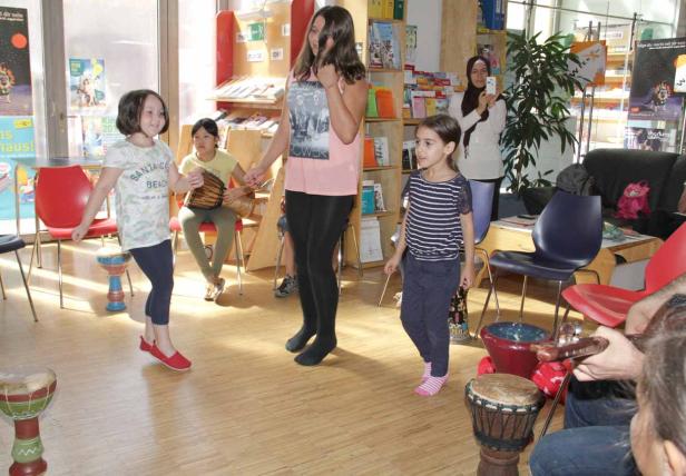 Eine Gruppe von Kindern tanzt und spielt auf Trommeln in einem Raum.