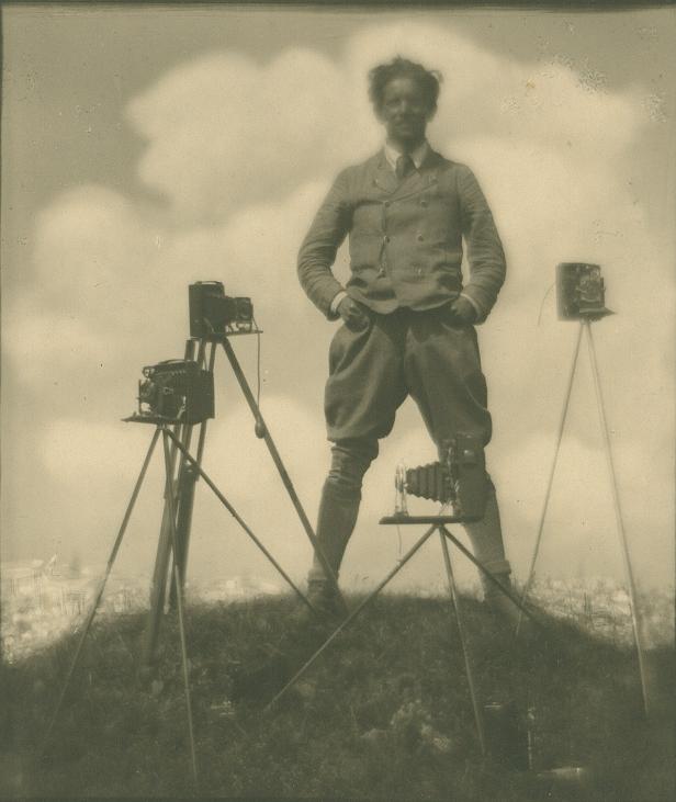Ein Fotograf steht mit drei alten Kameras auf Stativen im Freien.