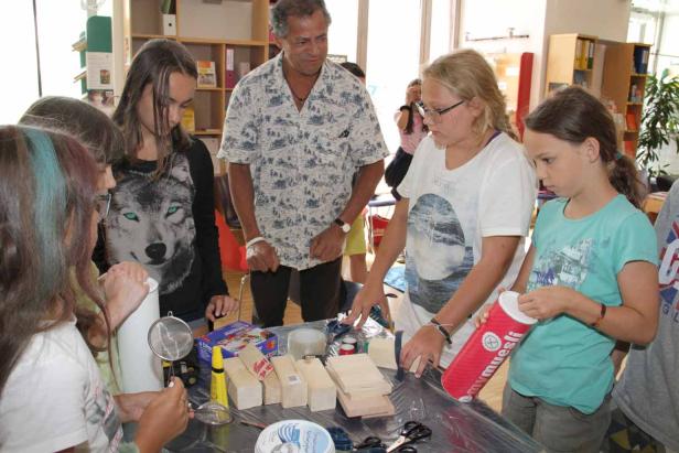 Eine Gruppe Kinder bastelt mit Holz, Klebstoff und anderen Materialien an einem Tisch.