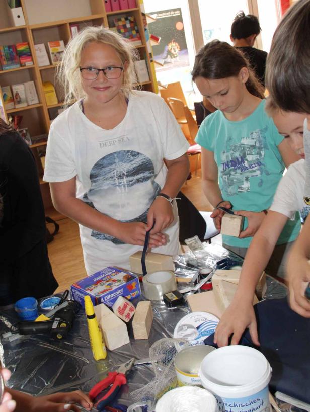 Kinder basteln mit Holz, Farbe und anderen Materialien an einem Tisch.