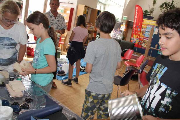 Eine Gruppe von Kindern bastelt mit Holz und Dosen in einem Raum.