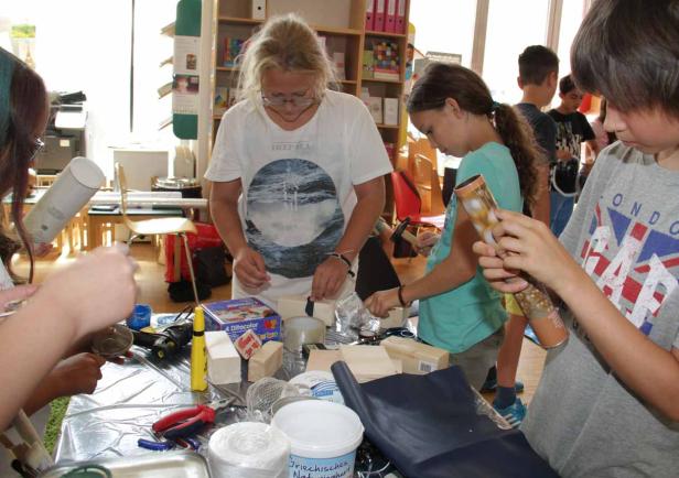 Eine Gruppe Kinder bastelt mit verschiedenen Materialien an einem Tisch.