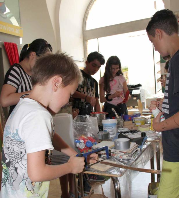 Eine Gruppe Kinder arbeitet an einem Tisch mit verschiedenen Werkzeugen und Materialien.