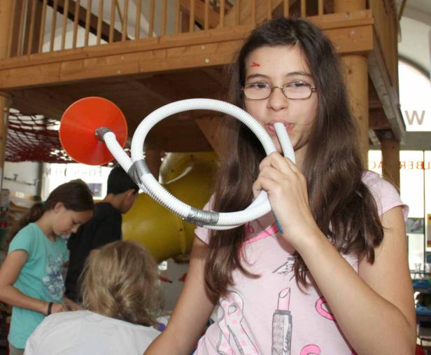 Ein Mädchen spielt mit einem selbstgebauten Musikinstrument aus Schlauch und Trichter.