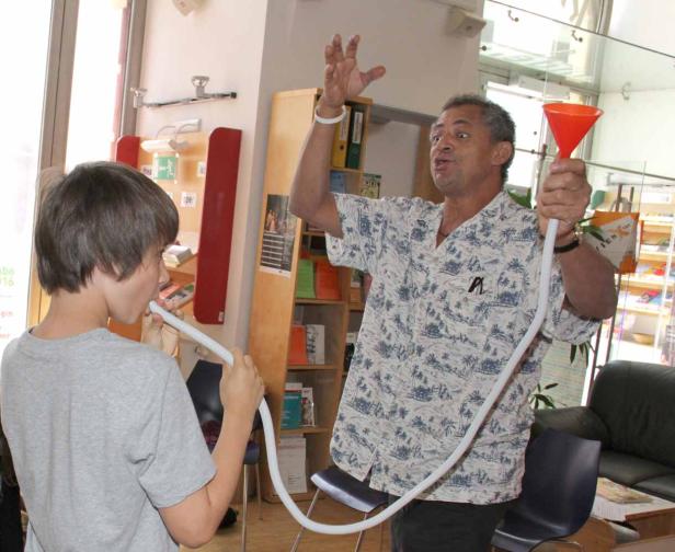 Ein Junge bläst in einen Schlauch, während ein Mann einen Trichter hält.