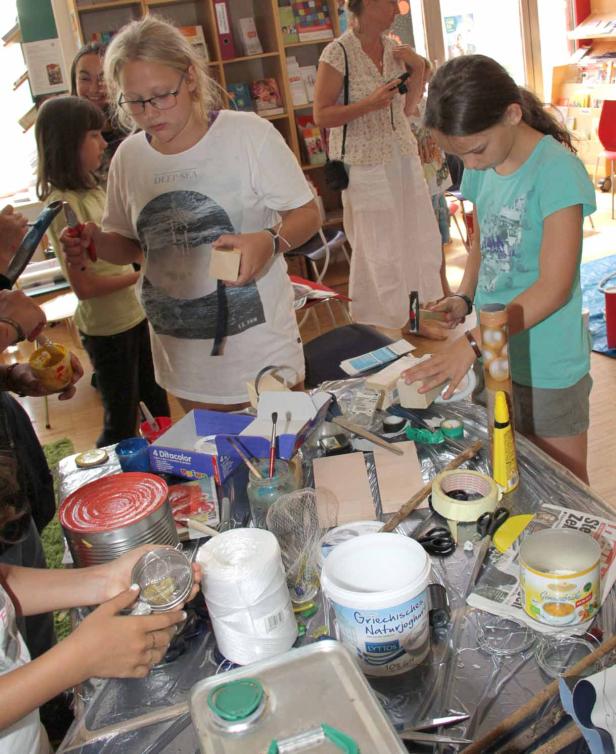 Kinder basteln an einem Tisch mit verschiedenen Materialien wie Dosen und Holzstücken.