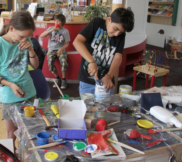 Kinder basteln an einem Tisch mit Farben und verschiedenen Materialien.