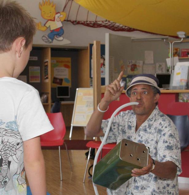 Ein Mann mit Hut führt einem Jungen ein selbstgebautes Blasinstrument vor.