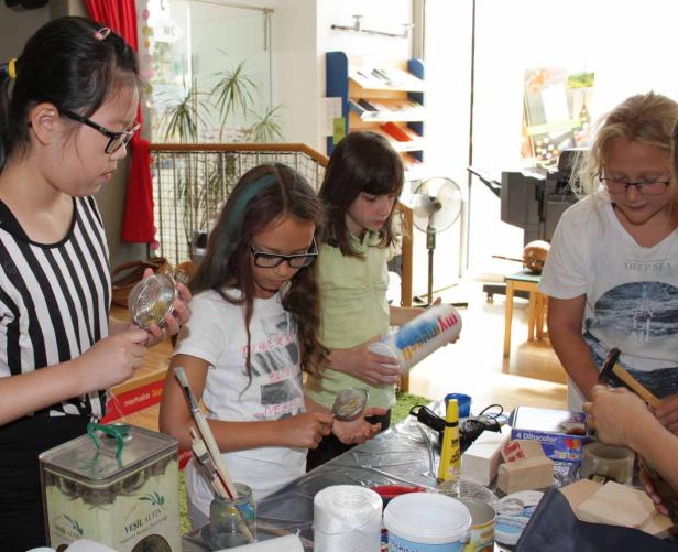 Vier Mädchen basteln an einem Tisch mit verschiedenen Materialien.