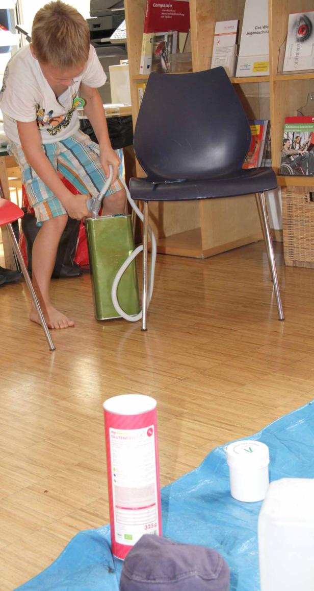 Ein barfüßiger Junge hantiert mit einem Schlauch an einem grünen Kanister.