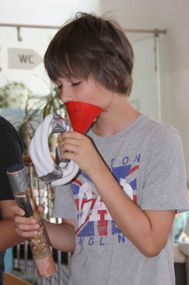 Ein Junge spielt mit einem selbstgebauten Instrument aus Trichter und Schlauch.