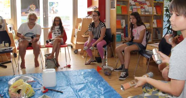 Eine Gruppe Kinder sitzt im Kreis und bastelt mit Dosen und anderen Materialien.