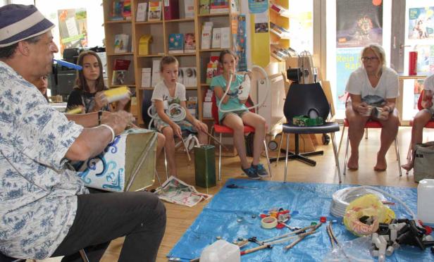 Eine Gruppe von Kindern und ein Mann bauen in einem Raum Musikinstrumente aus Recyclingmaterialien.