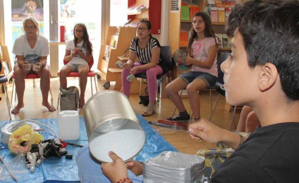 Eine Gruppe von Kindern und eine Frau sitzen in einem Raum und basteln mit Dosen und anderen Materialien.