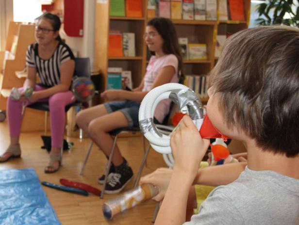 Ein Junge spielt mit einem selbstgebauten Instrument, während andere Kinder zusehen.