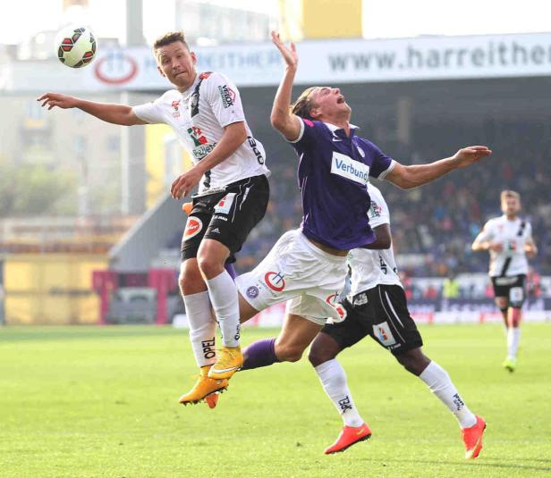 Zwei Fußballspieler springen auf dem Spielfeld, um einen Ball zu erreichen.