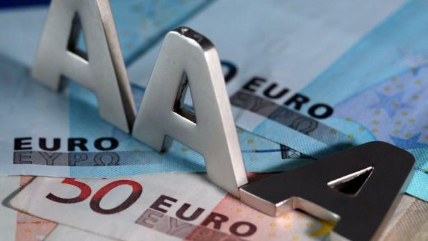 Drei silberne „A“-Buchstaben liegen auf Euroscheinen.