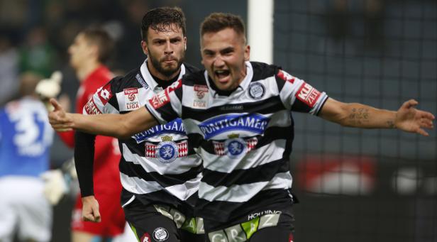 Zwei Fußballspieler in schwarz-weiß gestreiften Trikots jubeln mit ausgestreckten Armen.
