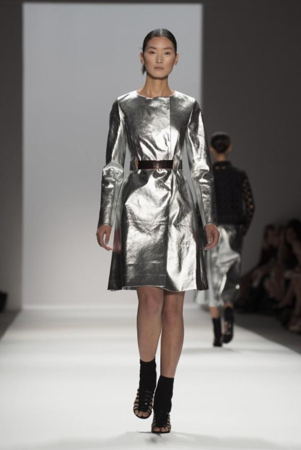 Eine Frau präsentiert ein silbernes Kleid mit Gürtel auf dem Laufsteg.