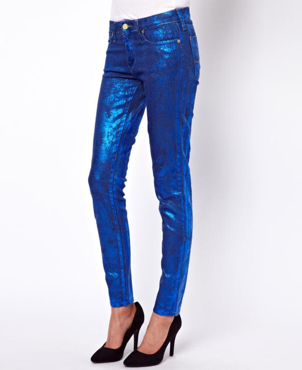 Eine Person trägt blaue, glänzende Jeans und schwarze High Heels.