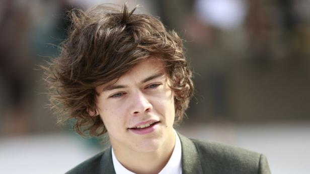 Porträt von Harry Styles mit braunen, lockigen Haaren und einem grauen Jackett.