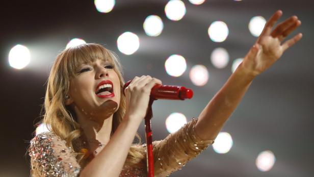 Taylor Swift singt mit einem roten Mikrofon in der Hand auf einer Bühne.