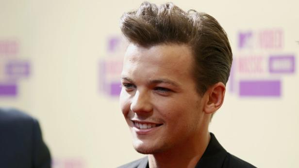 Louis Tomlinson lächelt auf einem roten Teppich.