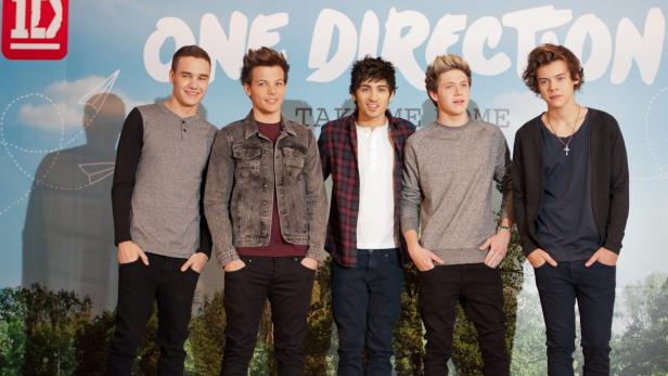 Die Boyband One Direction posiert vor einem Werbebanner.