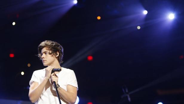 Harry Styles hält ein Mikrofon auf einer Bühne mit bunten Lichtern.