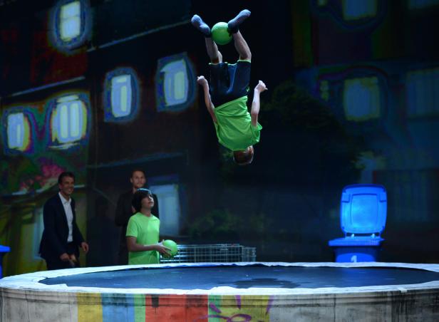 Ein Junge macht einen Salto auf einem Trampolin und hält einen Ball zwischen den Füßen.