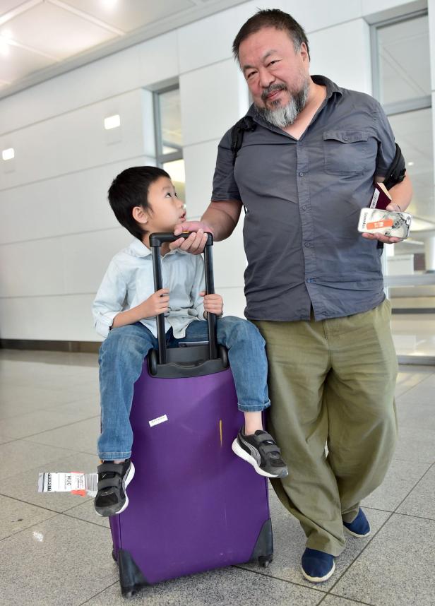 Ai Weiwei mit seinem Sohn auf einem lila Koffer in einem Flughafen.