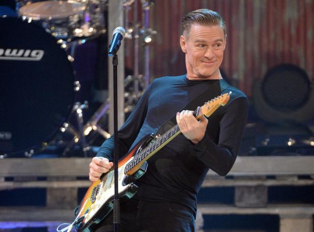 Bryan Adams spielt Gitarre auf einer Bühne.