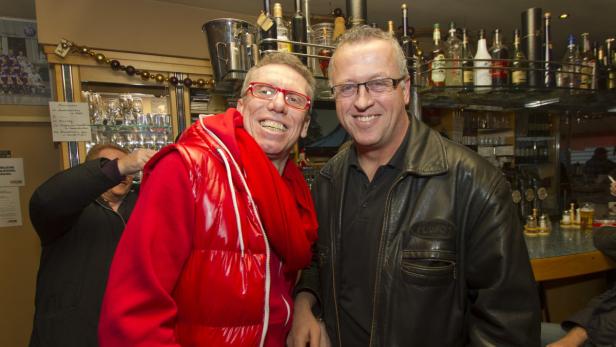Zwei Männer stehen lächelnd in einer Bar nebeneinander.