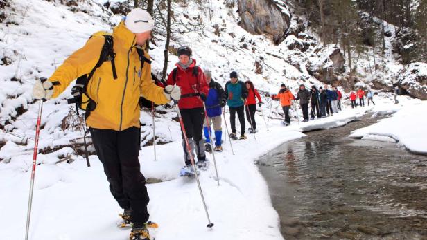 Eine Gruppe von Menschen wandert mit Schneeschuhen entlang eines verschneiten Flusses.
