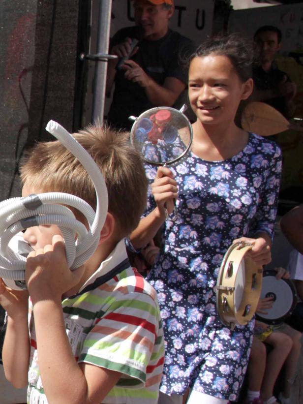 Kinder musizieren mit ungewöhnlichen Instrumenten wie einem Schlauch und einem Sieb.