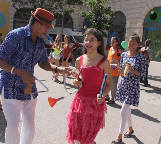Ein Mann mit Hut gibt zwei Mädchen Musikinstrumente auf der Straße.