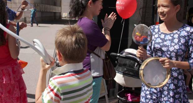 Eine Gruppe von Kindern und Erwachsenen macht Musik mit verschiedenen Instrumenten wie Triangeln und Tamburinen.