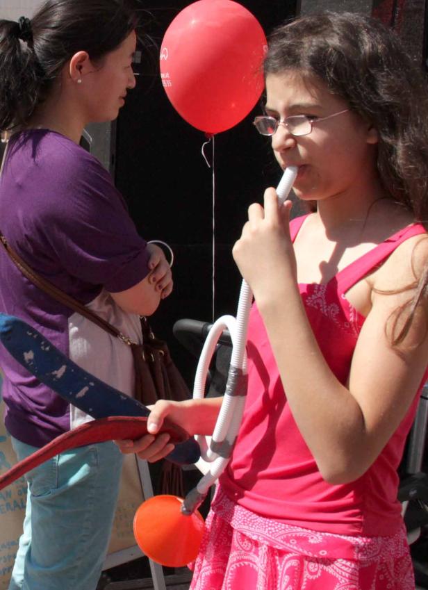 Ein Mädchen mit Brille bläst in ein Spielzeug, während eine Frau daneben steht.