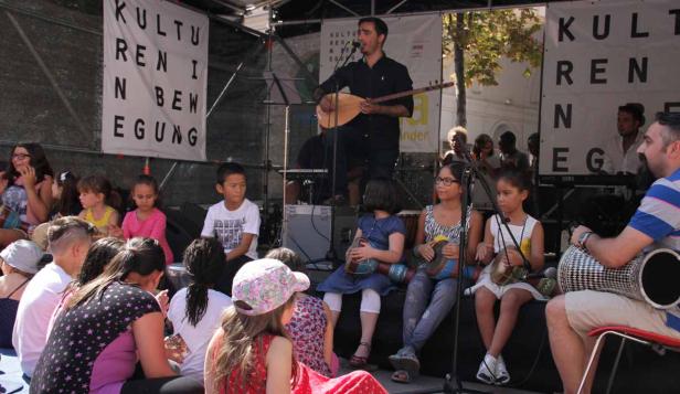 Ein Mann spielt Saz vor einer Gruppe von Kindern bei einer Veranstaltung der „Kulturen in Bewegung“.