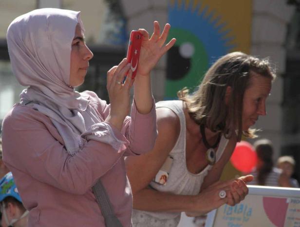 Eine Frau mit Kopftuch fotografiert mit einem Smartphone, auf dessen Rückseite eine türkische Flagge abgebildet ist.