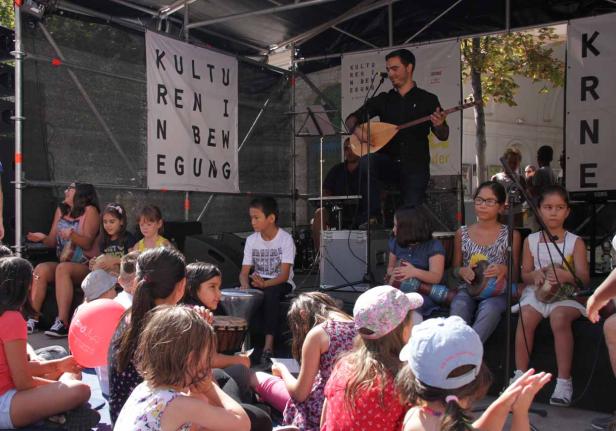 Ein Mann spielt Saz vor einer Gruppe von Kindern bei einer Kulturveranstaltung.
