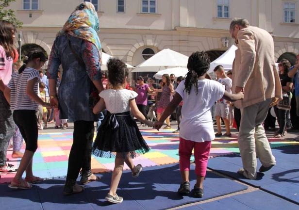 Eine Gruppe von Kindern und Erwachsenen tanzt Hand in Hand auf einem Platz.